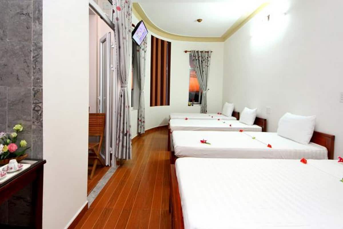 A hotel room with four single beds, a TV, a wooden floor, and a small table with a floral arrangement.
