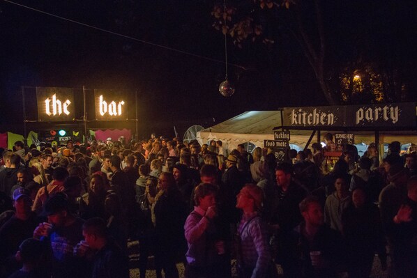 A crowded outdoor event with illuminated signs for 'the bar' and 'kitchen party'. - Oktoberfest and Springfest All Inclusive Camping (Munich)