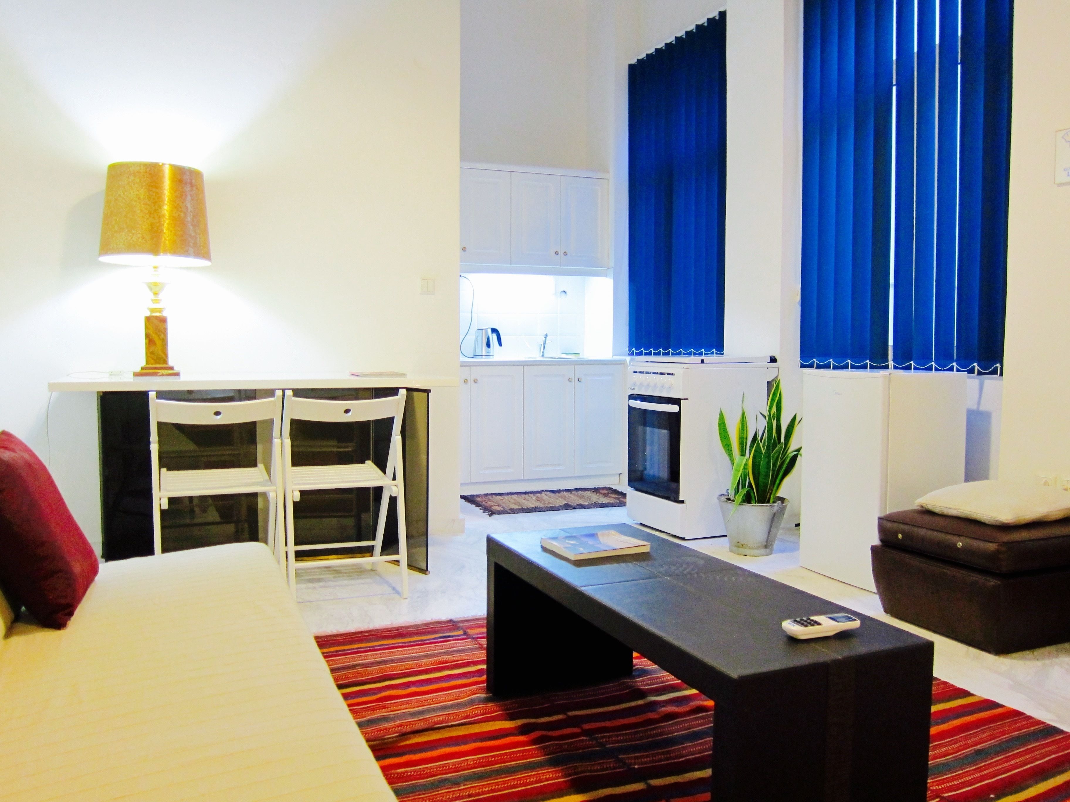 Een knus verblijf met een bed, een bureau met stoelen, een kitchenette, een bijzettafeltje en een potplant.