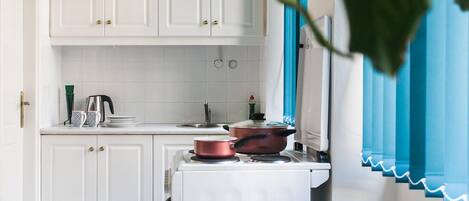 A kitchen with white cabinets, a stove, and a pot on the counter.