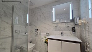Une salle de bain moderne avec une douche à parois de verre, des toilettes, un lavabo avec un miroir au-dessus et un porte-serviettes.