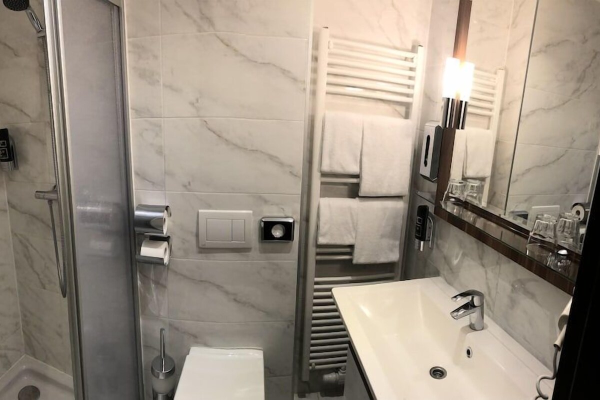 A bathroom with a glass shower enclosure, a sink, a towel rack, and a mirror.