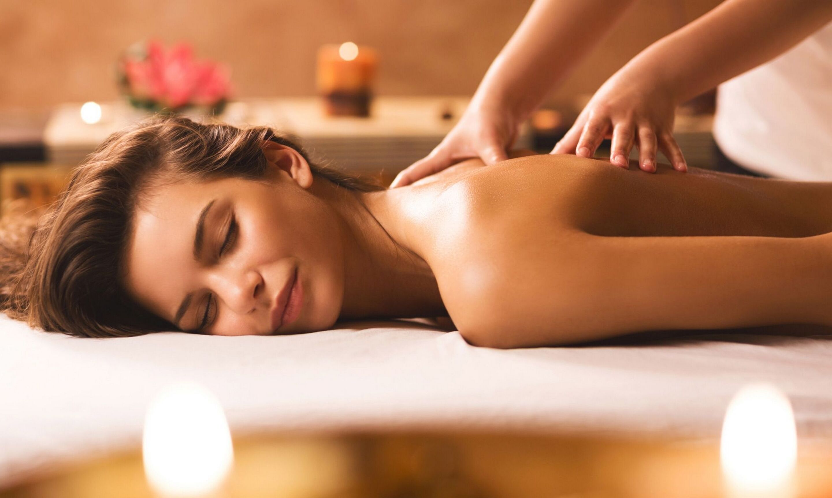 A person receiving a massage on a massage table with candles in the background.