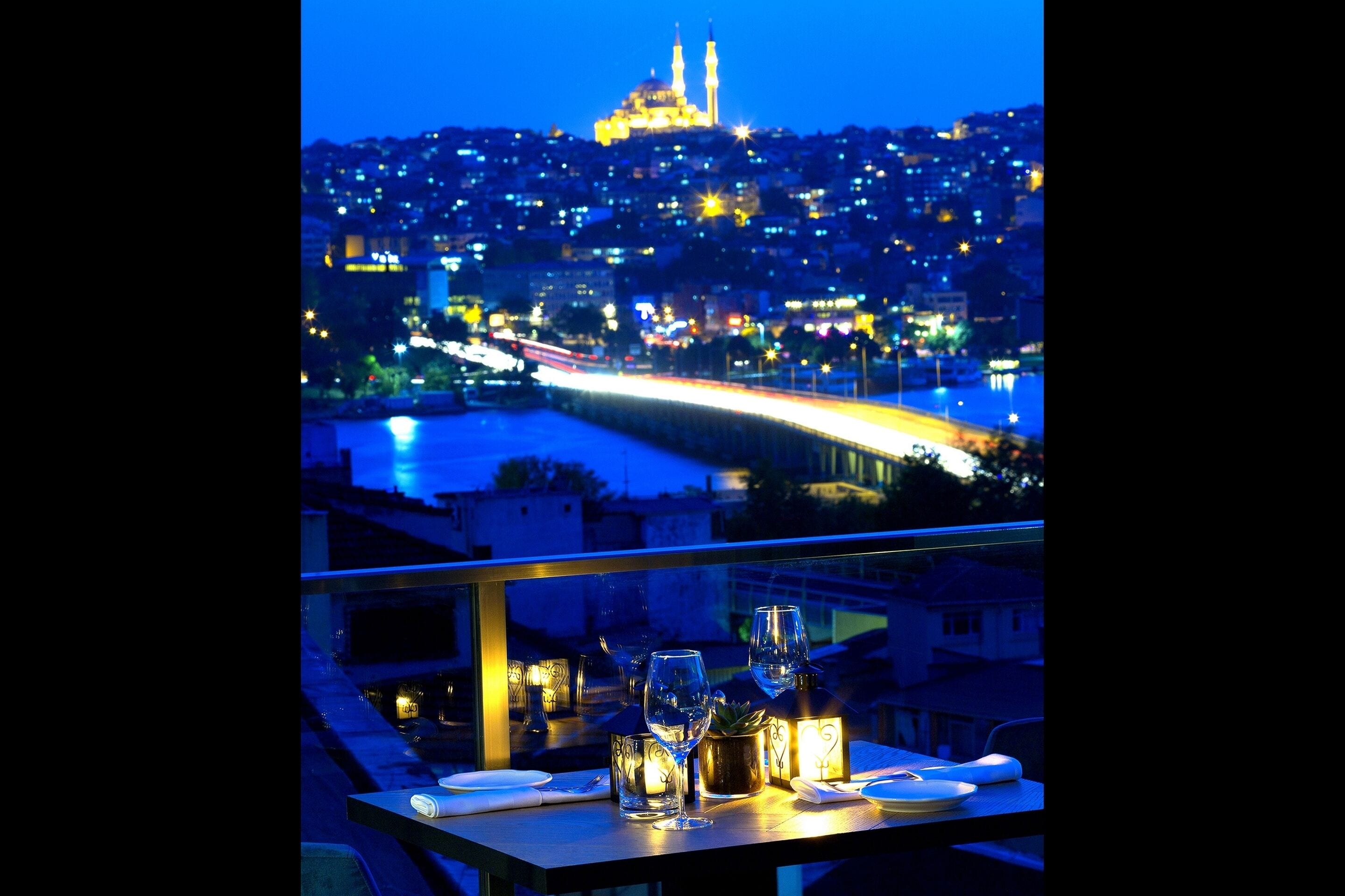 A table with glasses and a bottle, overlooking a cityscape with a river and a bridge at night.