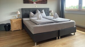 A modern bedroom with a large bed, two bedside tables, a nightstand, a window with curtains, and a wall-mounted artwork. - Landhotel Krone (Oberreute)