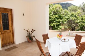 A balcony with a table set for two, a potted plant, and a view of a mountainous landscape. - Villa Vlatos (Kissamos)