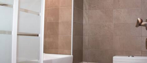 A bathroom with a toilet, a sink, a trash bin, and a shower area.
