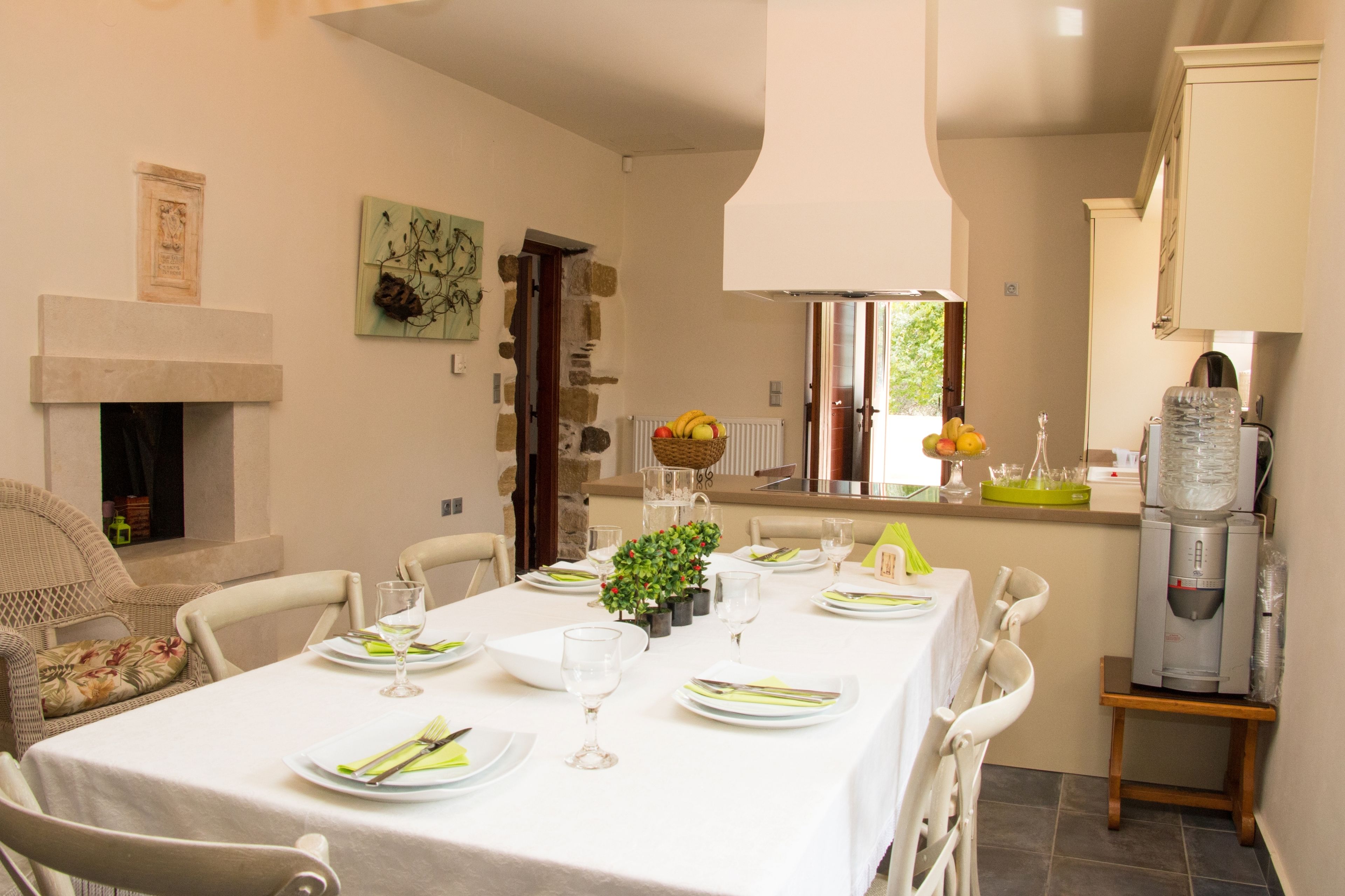 A dining area with a table set for four, a fireplace, stone walls, and a kitchen area with a water dispenser.