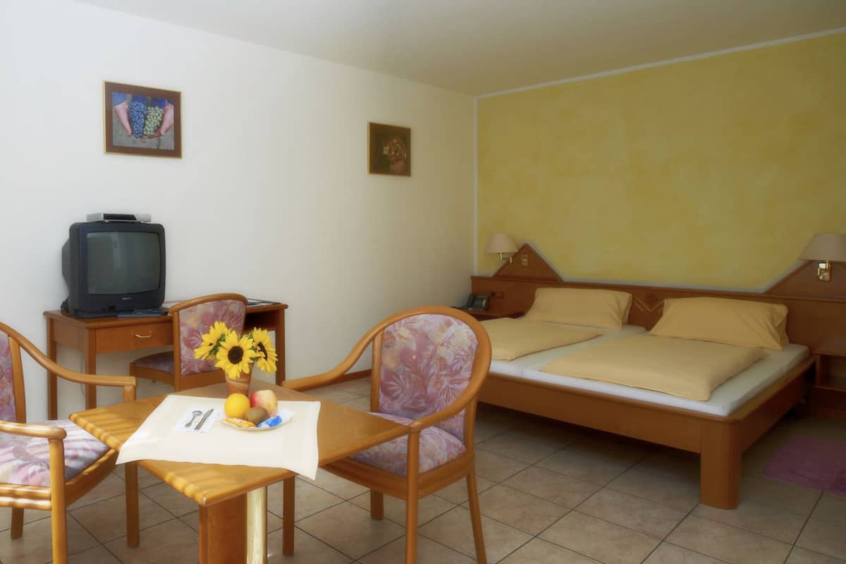 A hotel room with a bed, a TV, a dining table with chairs, and a small table with a vase of flowers.