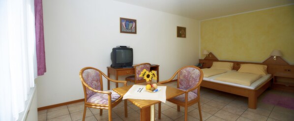 A hotel room with a bed, a TV, a dining table with chairs, and a small table with a vase of flowers. - Gasthof Löwen (Breisach)