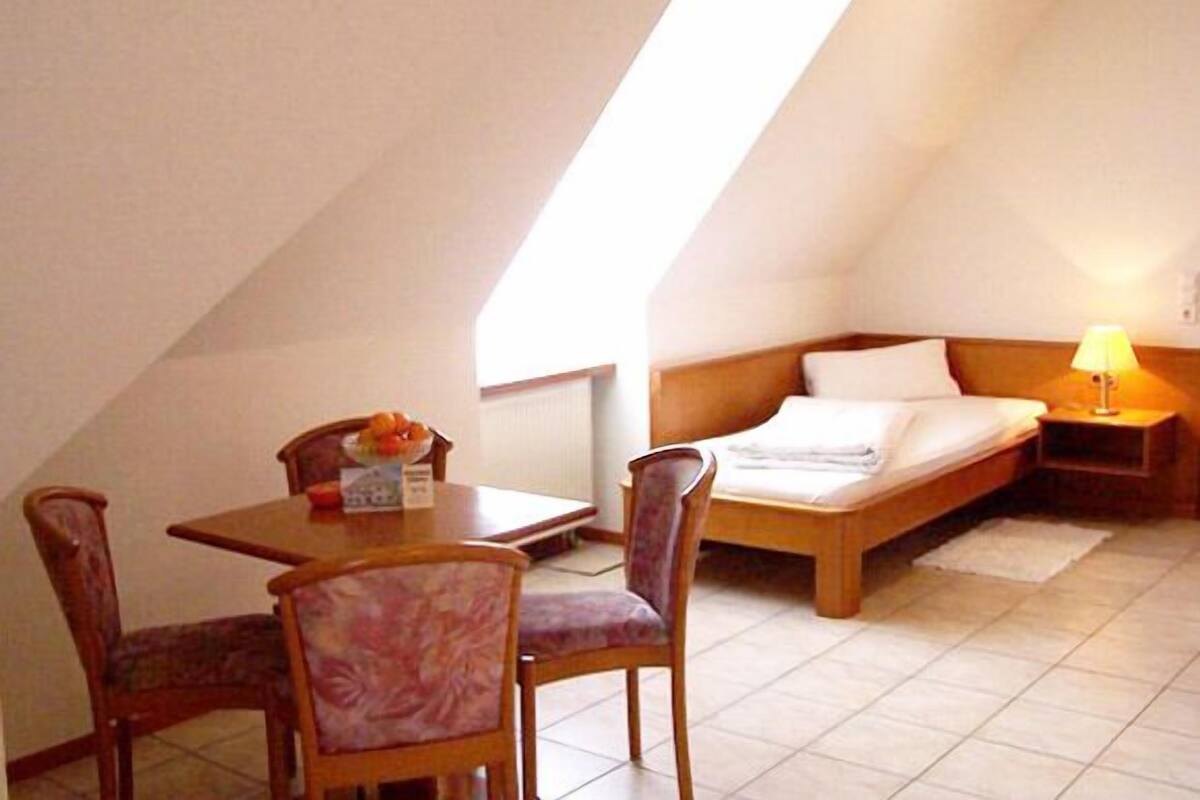 A small, cozy room with a bed, a table, and two chairs.