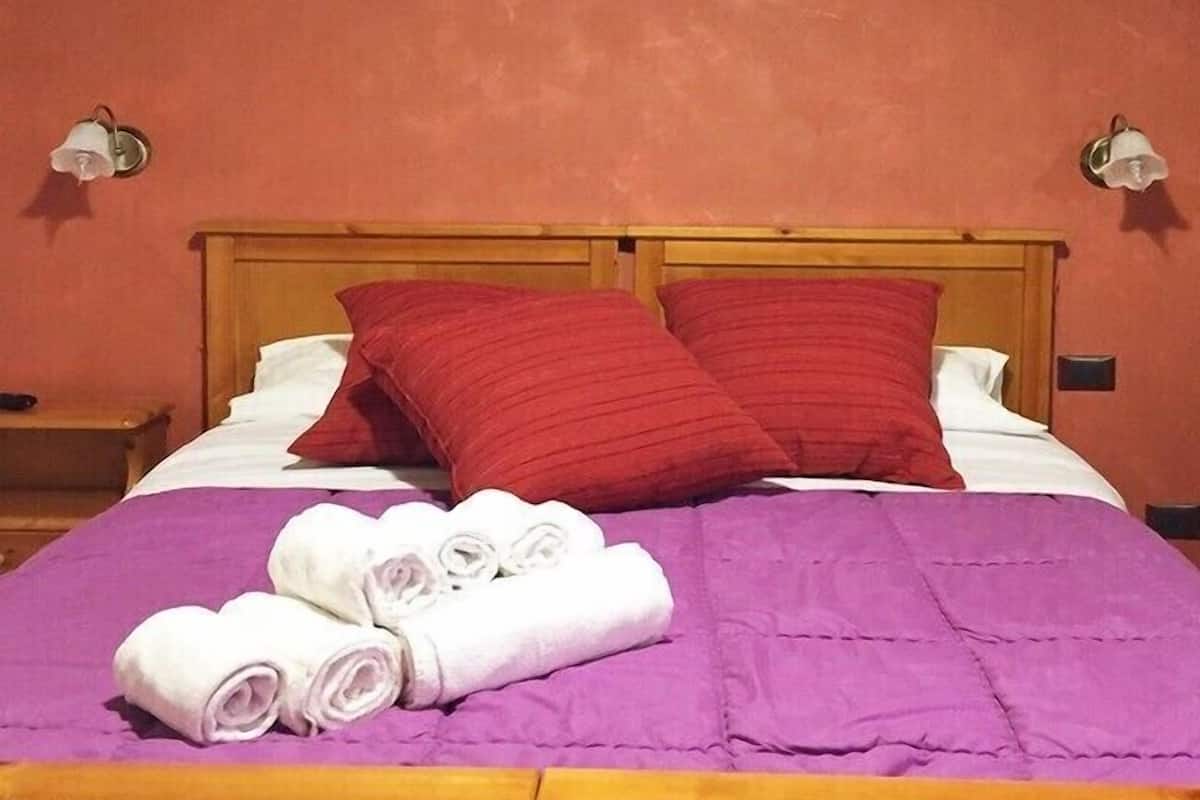 Een bed met een houten hoofdbord, rode kussens, een paarse deken en opgerolde witte handdoeken.