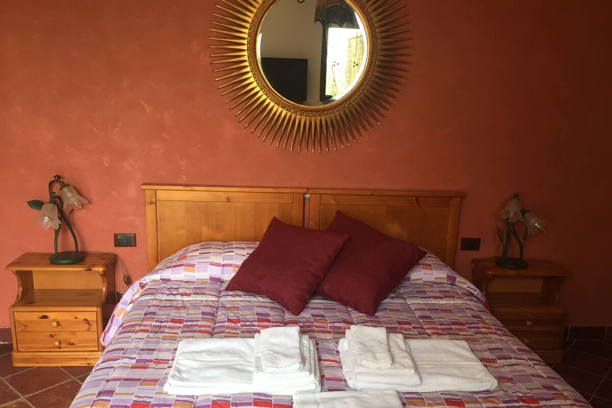 Een net opgemaakt bed met een kleurrijke quilt, twee kussens en opgevouwen handdoeken op een houten hoofdbord.