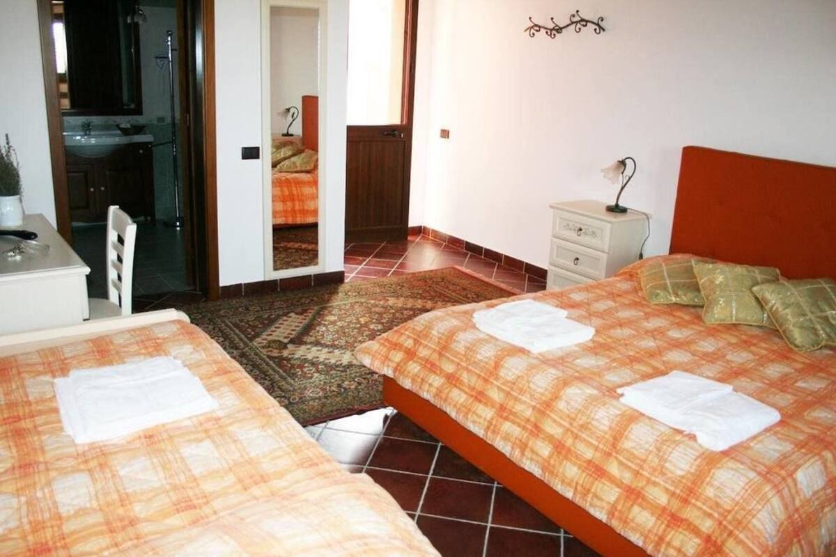 Een slaapkamer met twee bedden, een nachtkastje, een dressoir en een badkamer zichtbaar door een open deur.