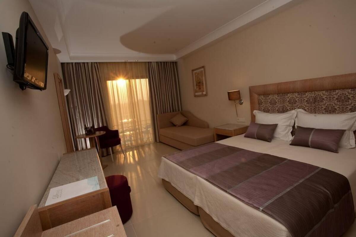 A hotel room with a large bed, a desk, a chair, a TV, and a window with curtains.