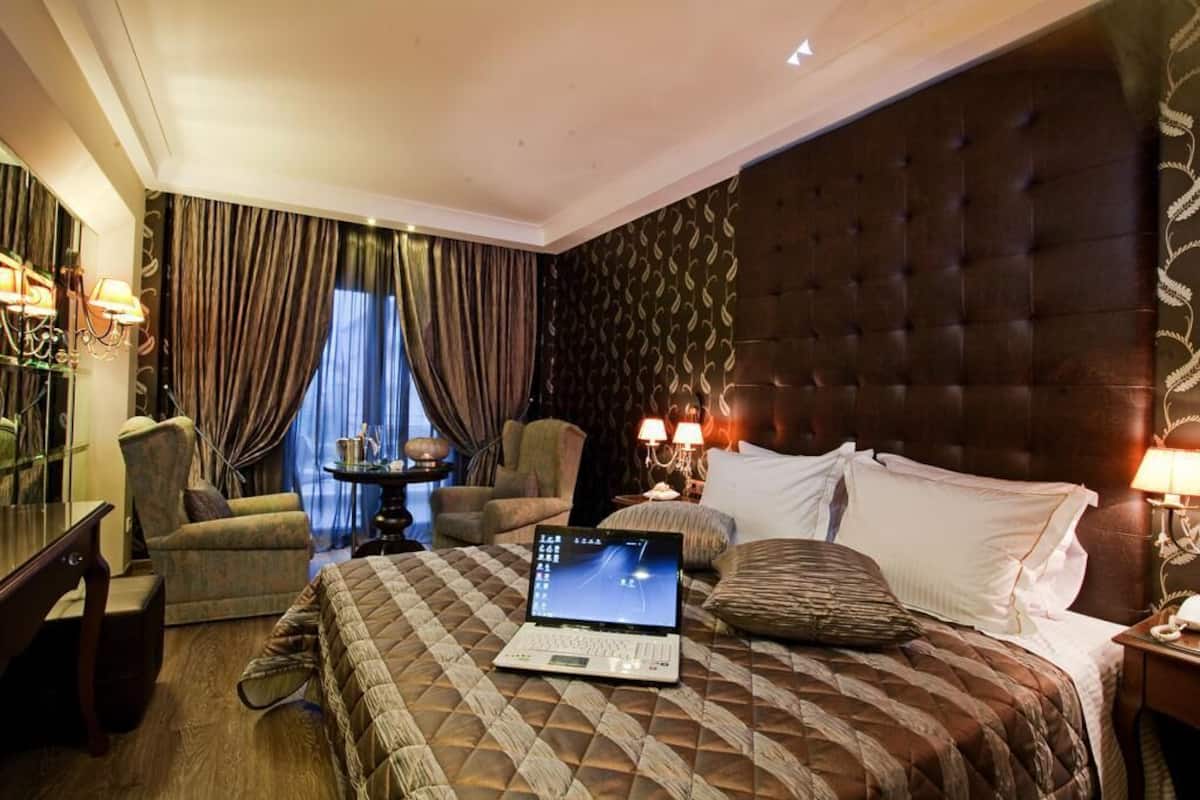 A hotel room with a large bed, a laptop on the bed, a chair, a small table, and a lamp.