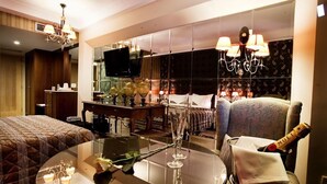 A hotel room with a bed, a round table with a glass top, a television, a minibar, and a large mirror. - Danai Hotel & Spa (Katerini)