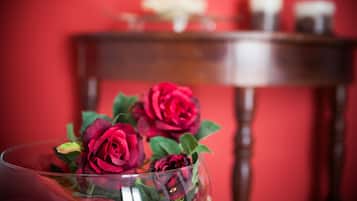 A glass vase with red roses on a table against a red wall.