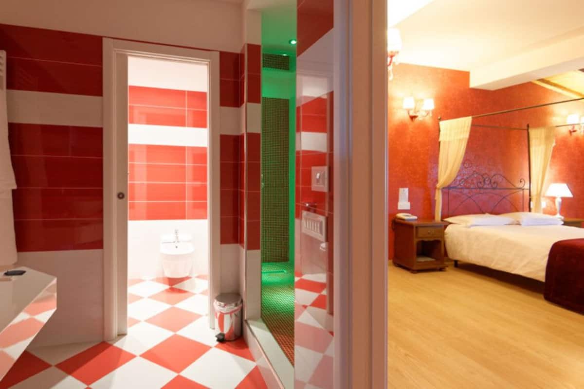 A hotel room with a checkered floor, a large mirror, a sink, a bed, and a nightstand with a lamp.