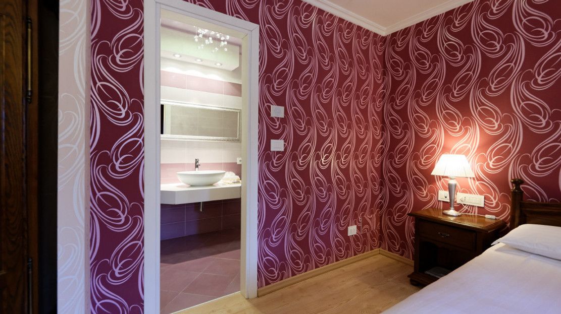 A hotel room with a vanity, a bed, and a nightstand with a lamp.