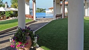Un espacio exterior techado con piscina, columnas blancas y una planta en maceta.