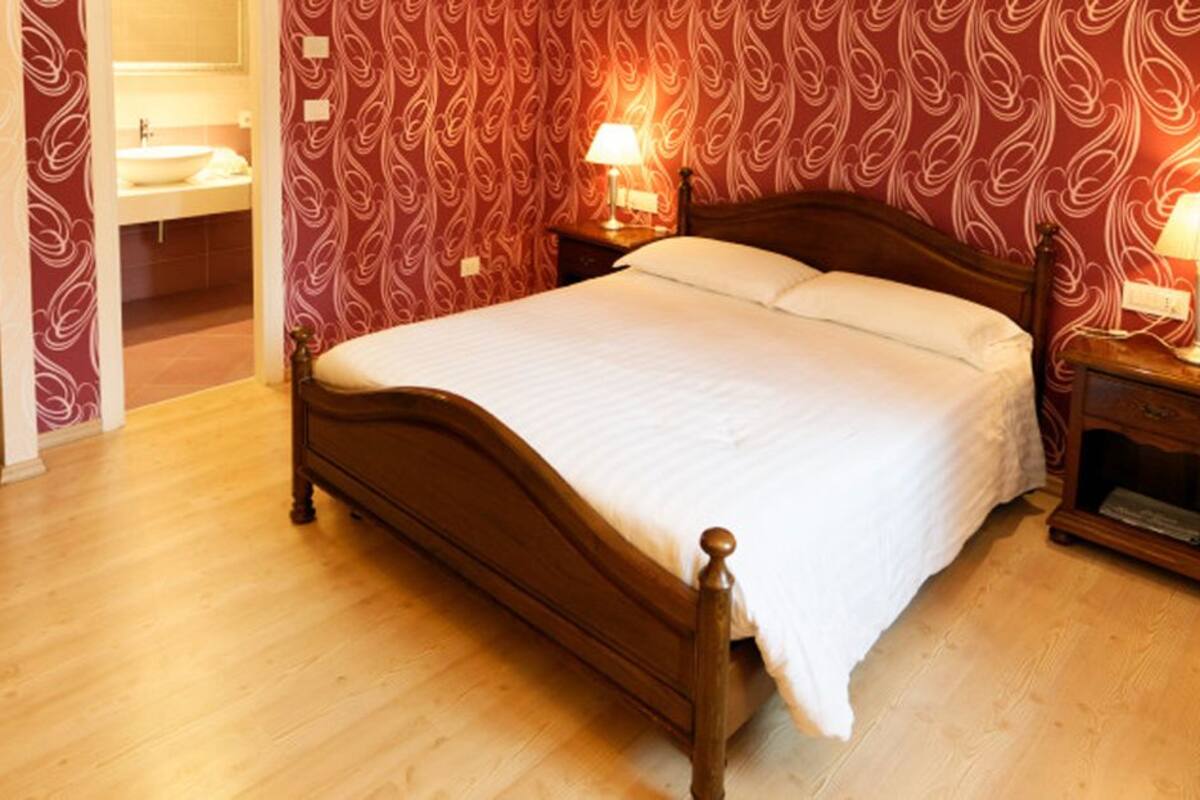 A bedroom with a wooden bed, two bedside lamps, and a red patterned wallpaper.