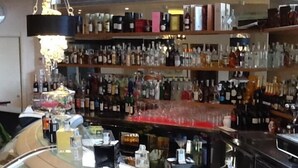 Zona de bar con estanterías llenas de botellas y una vitrina con pasteles.