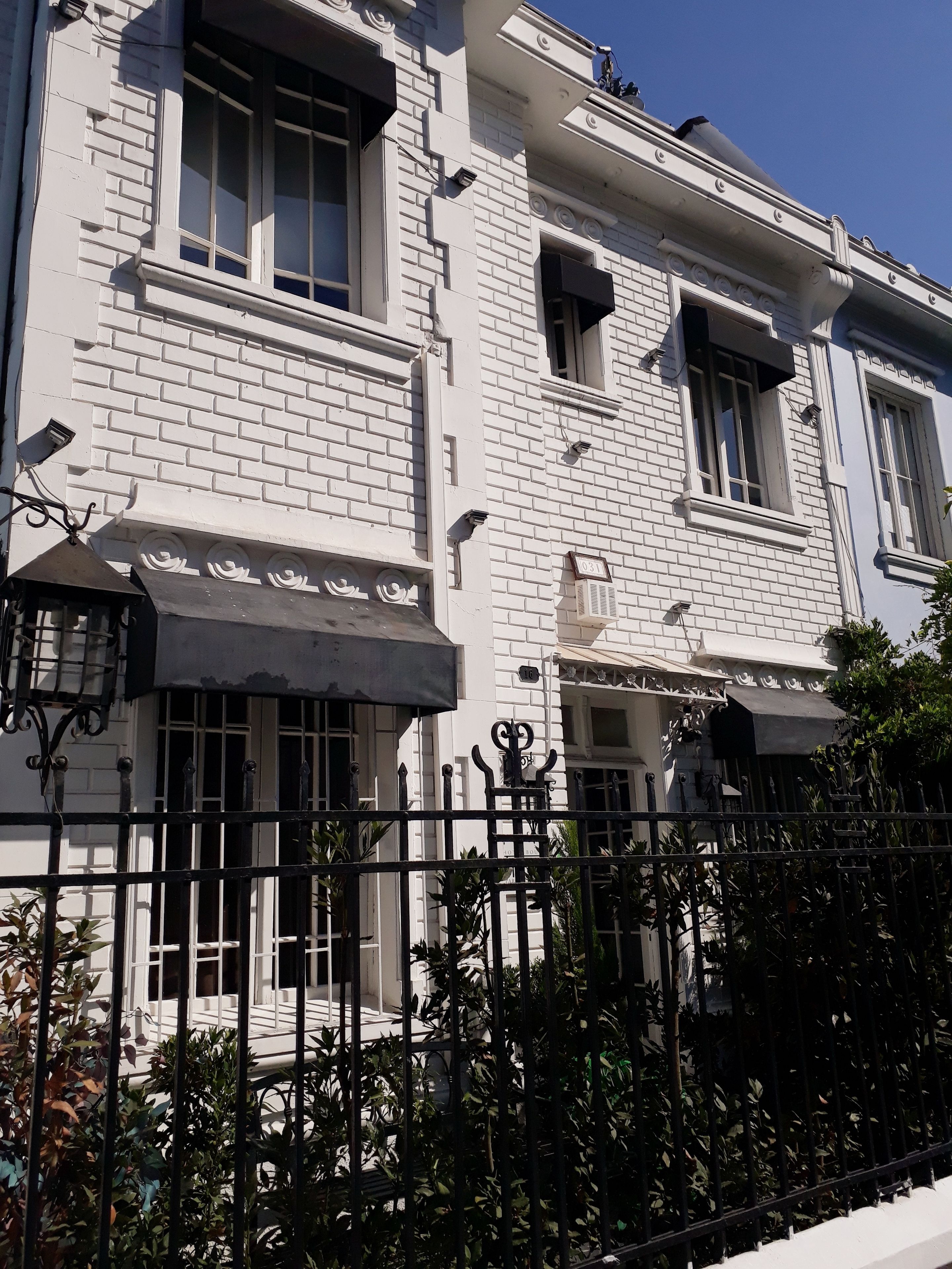 Un edificio blanco con varias ventanas, una cerca de metal negro y algunas plantas en la fachada.