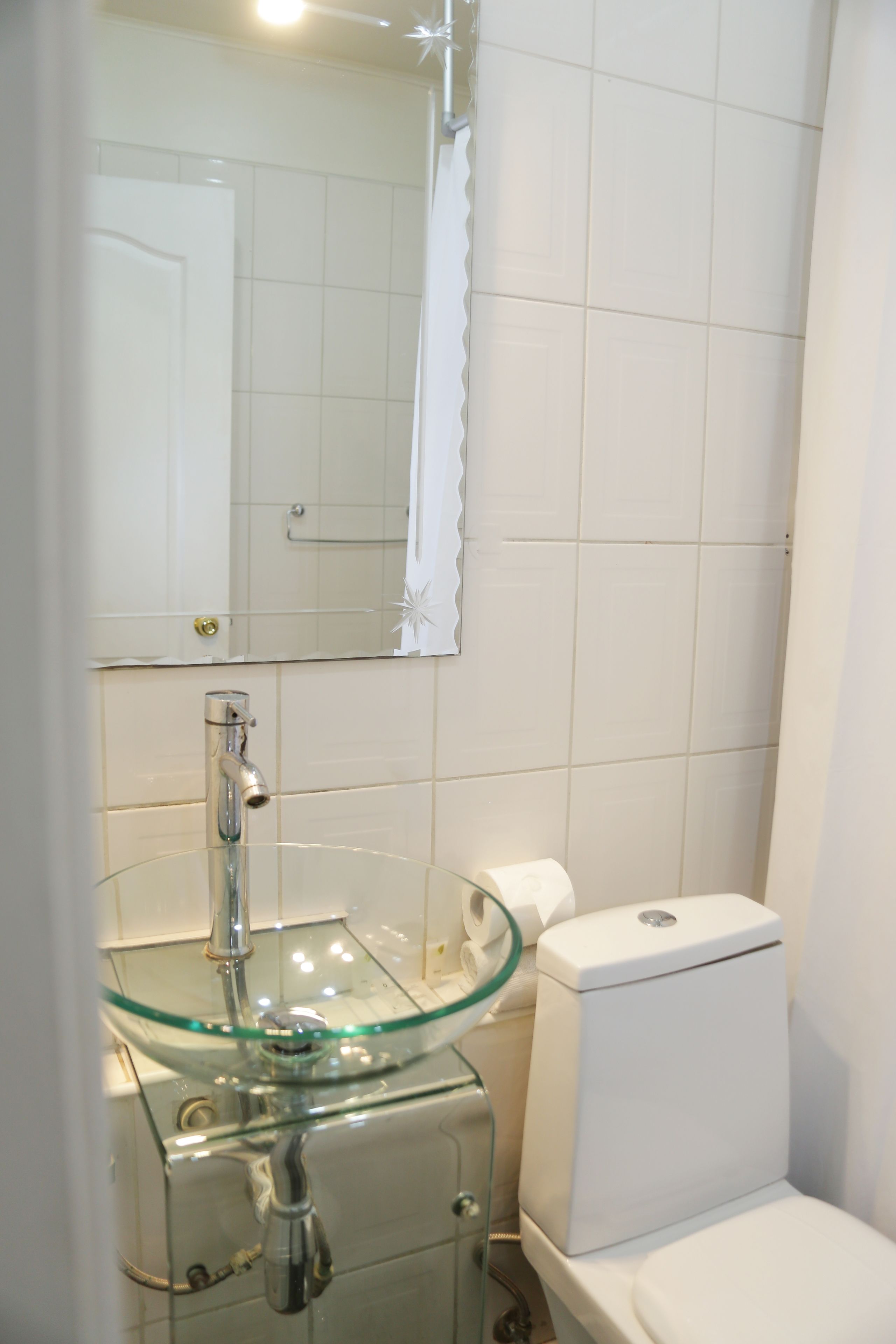 Ein Badezimmer mit einem Waschbecken aus Glas, einer Toilette und einem Spiegel.