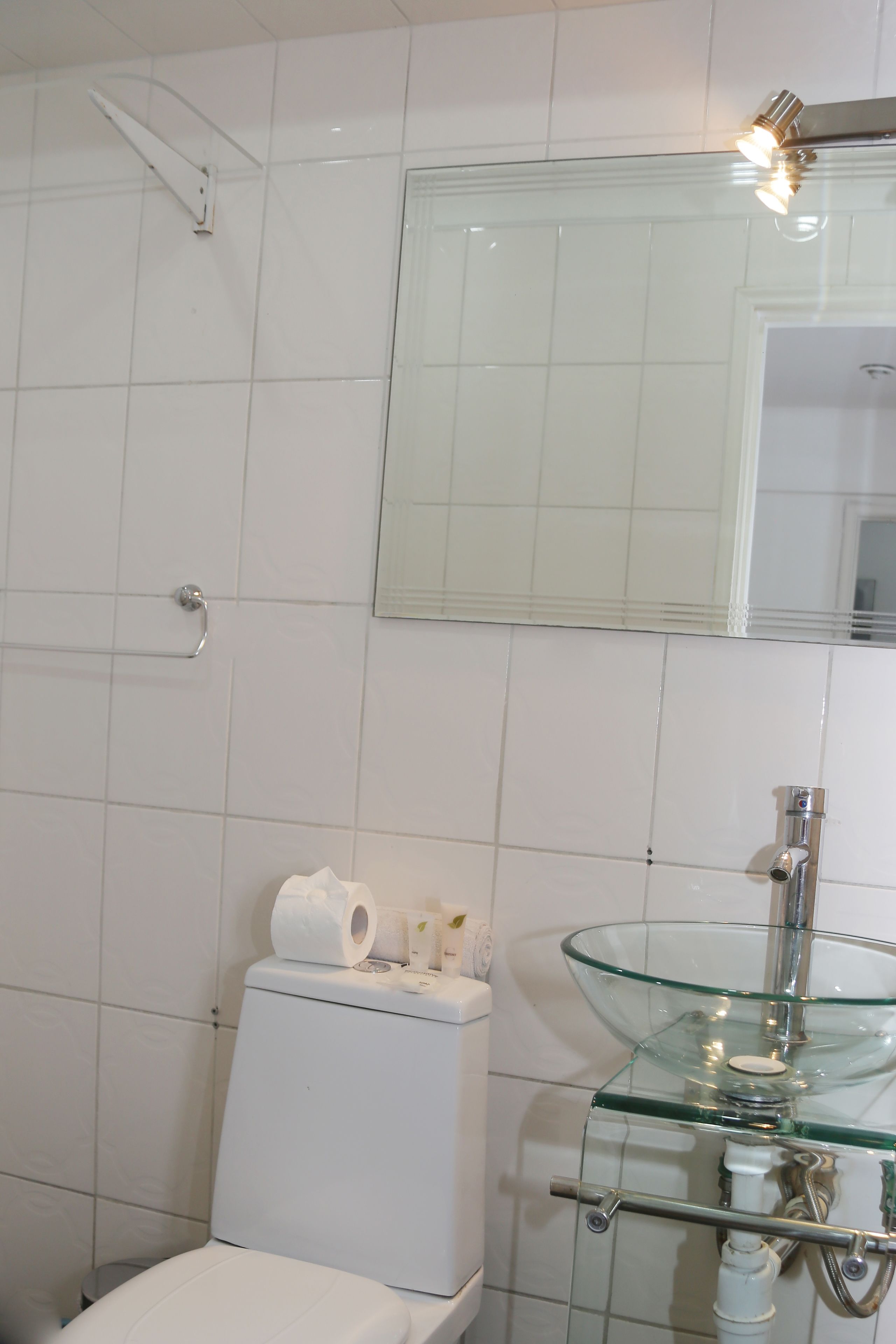 A bathroom with white tiles, a glass sink, and a toilet.