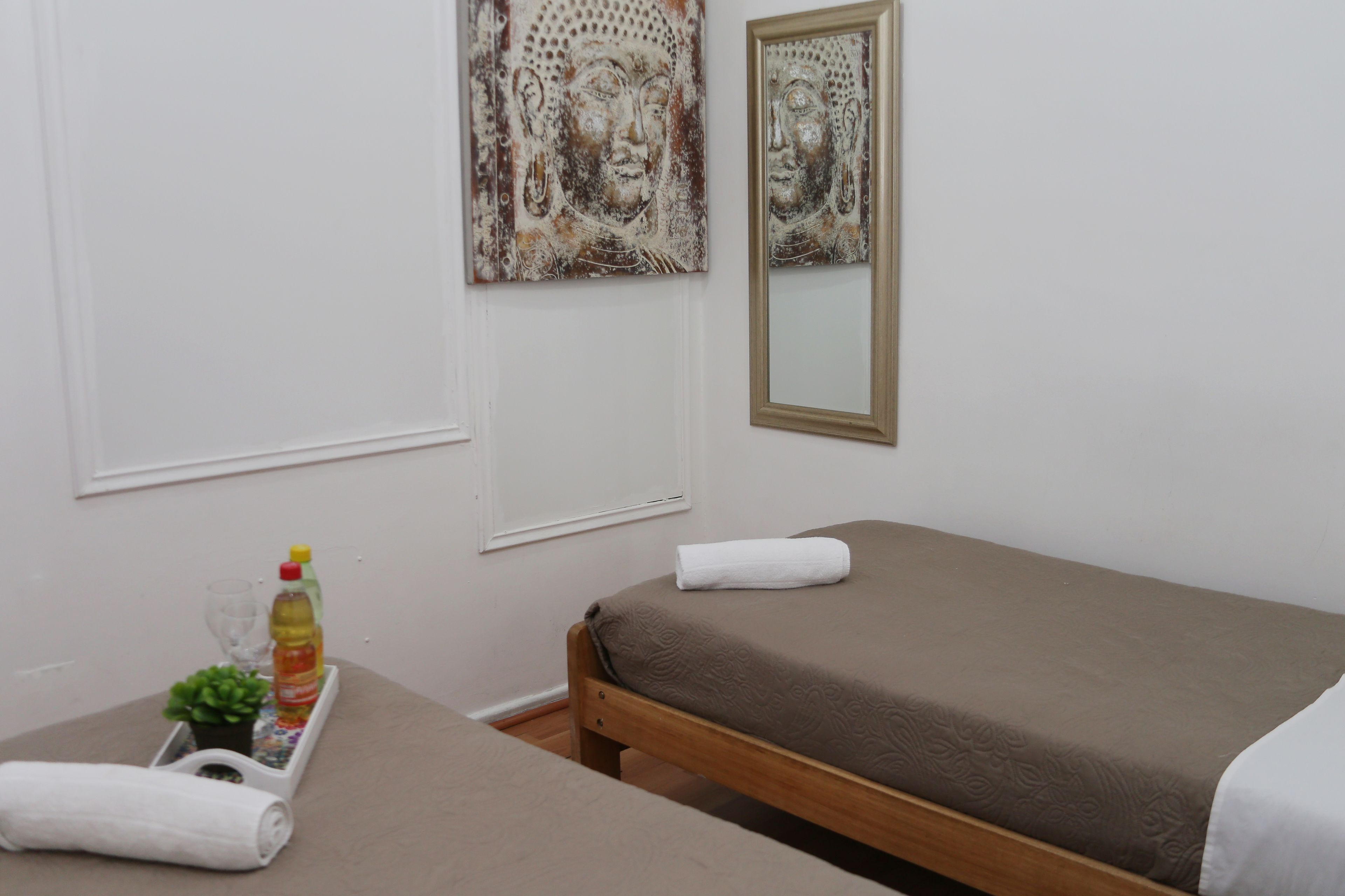 A room with two beds, a small table with toiletries, and artwork on the walls.