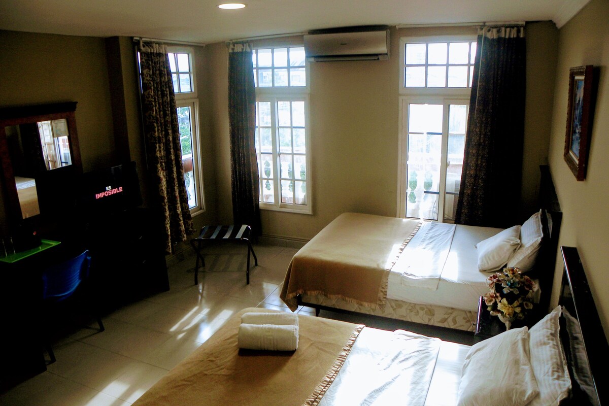 A hotel room with two beds, a desk, a chair, and a television.