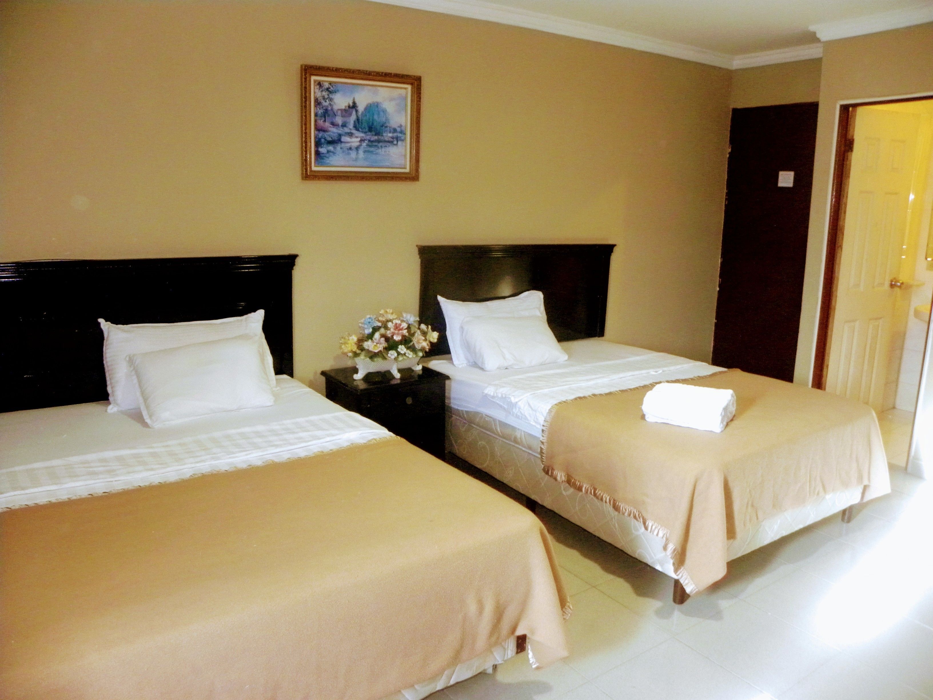A hotel room with two beds, a nightstand with a vase of flowers, and a painting on the wall.