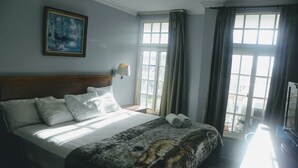 A hotel room with a large bed, a painting on the wall, a window with curtains, and a view of the outside. - Hotel Meryland (Colon)
