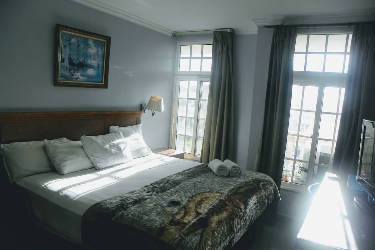 Ein Hotelzimmer mit einem großen Bett, einem Bild an der Wand, einem Fenster mit Vorhängen und Blick nach draußen.