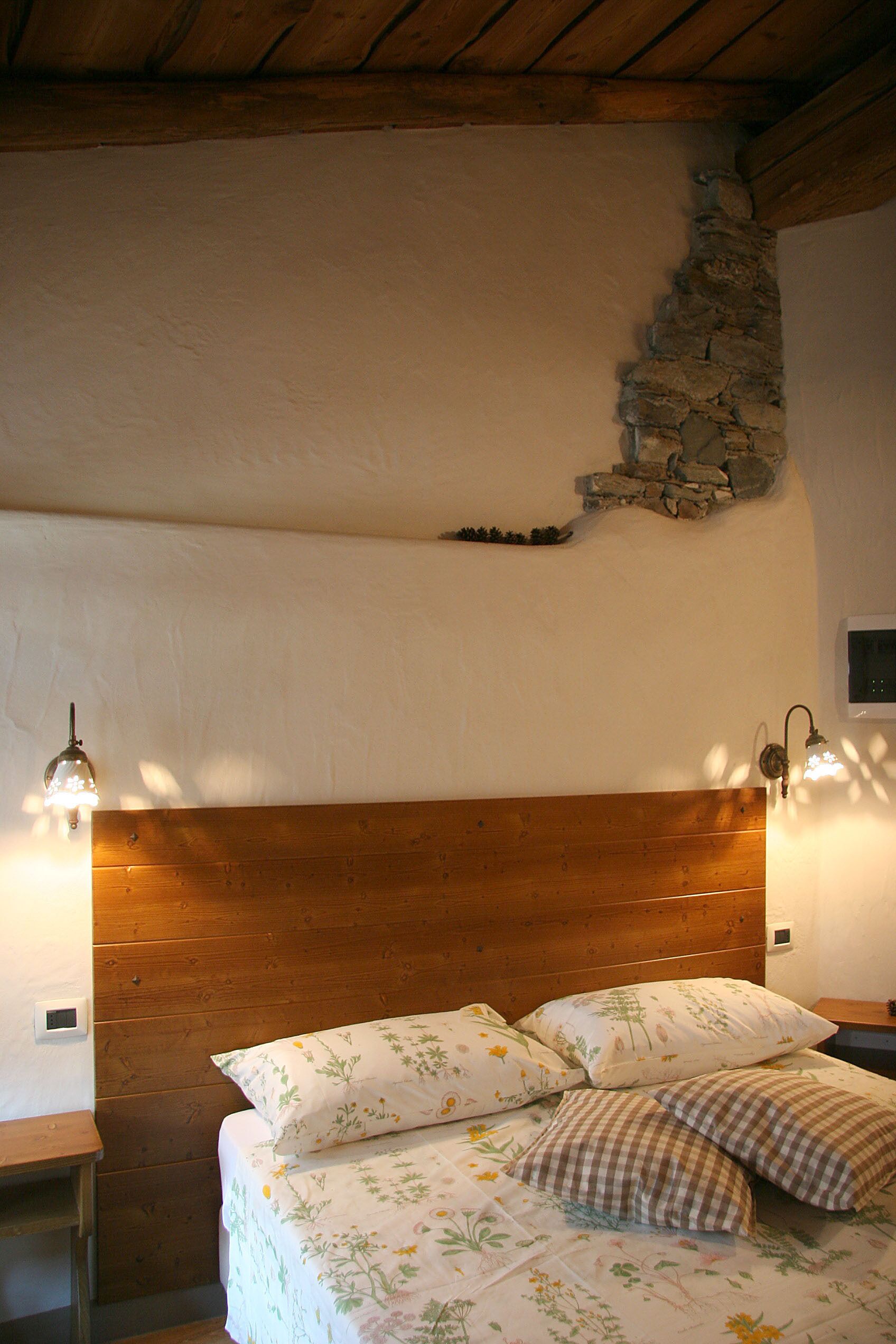 A bedroom with a wooden headboard, floral bedding, and two wall-mounted lamps.