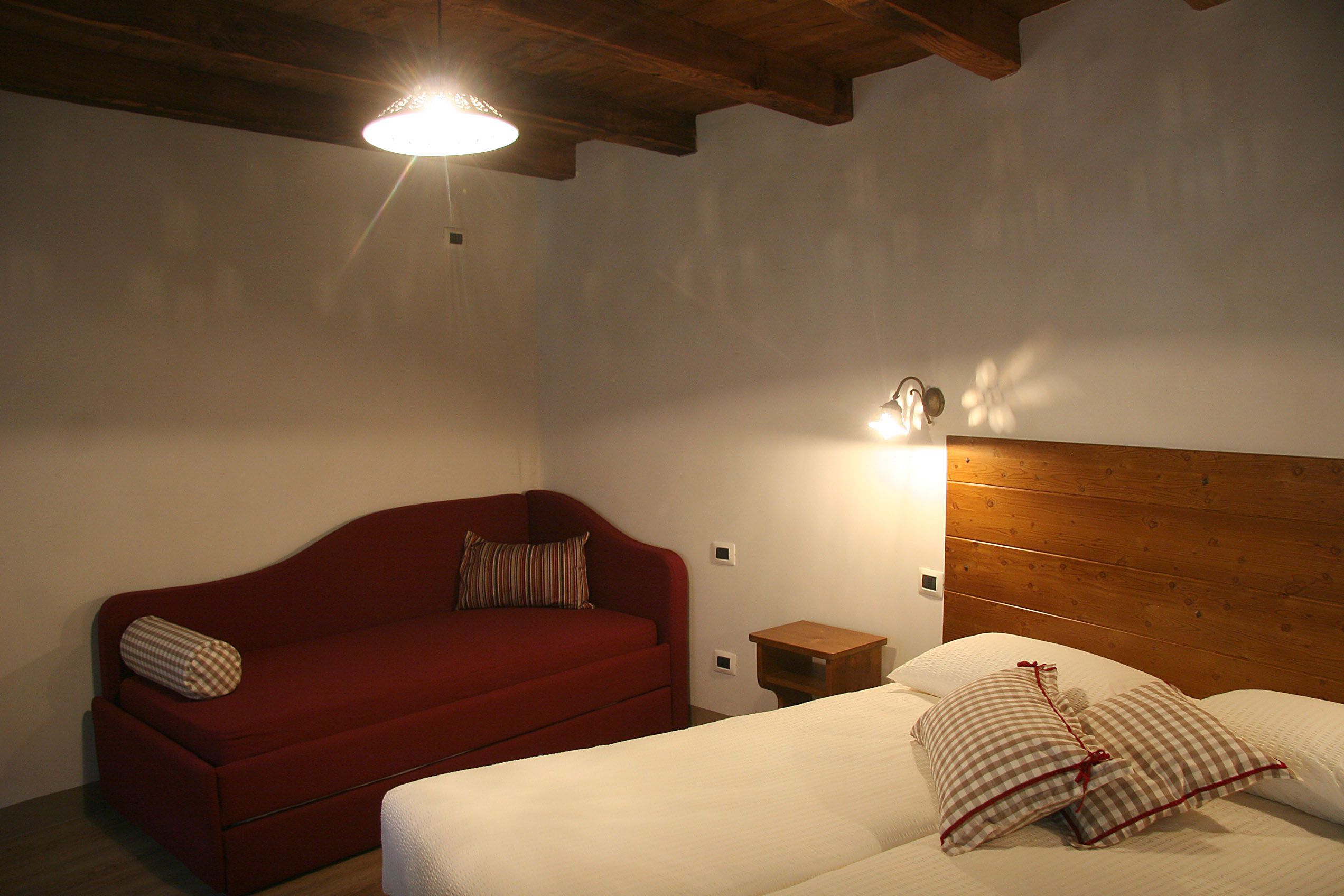 A bedroom with a wooden headboard, a red sofa, and a white bed with checkered pillows.