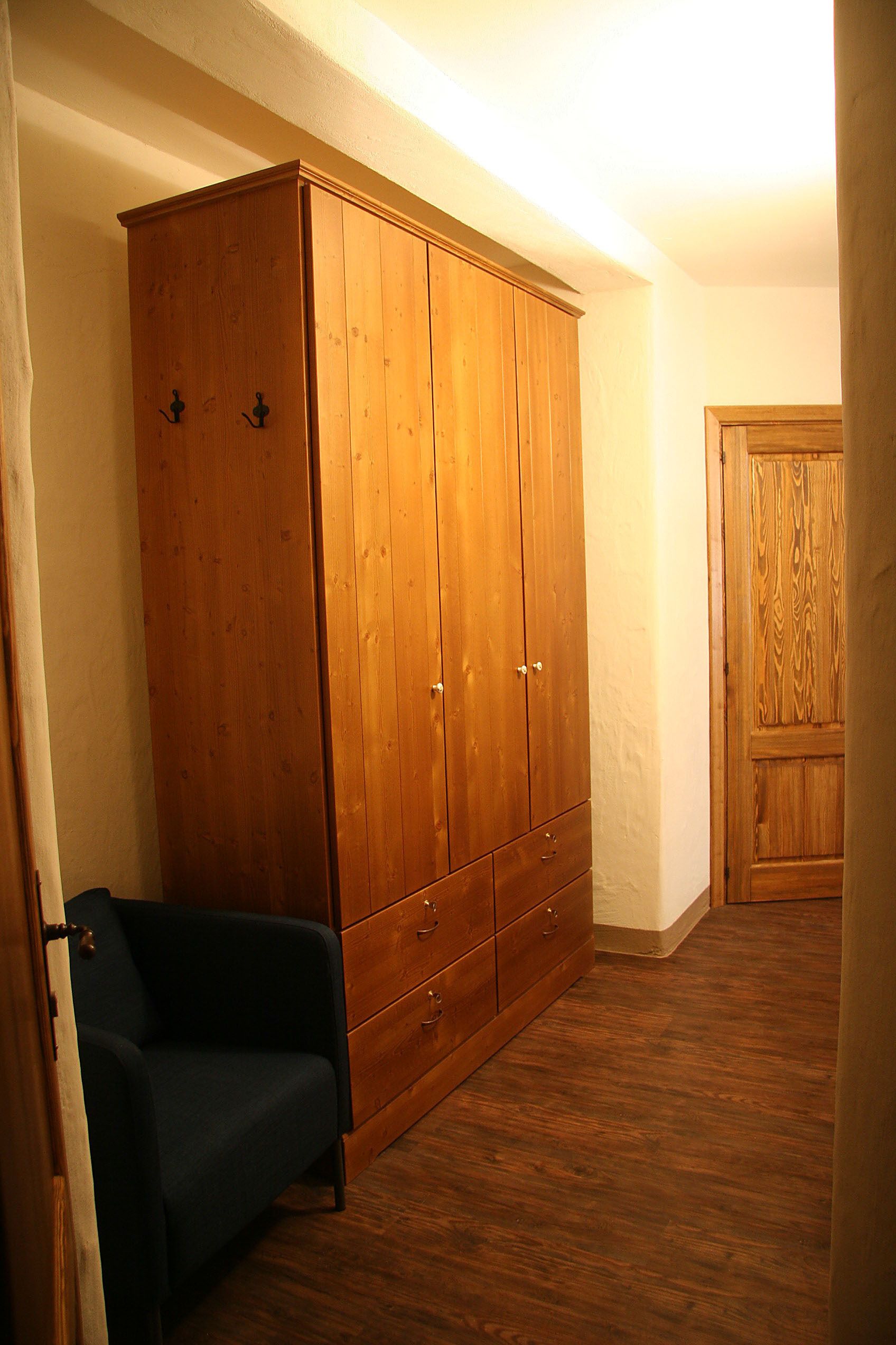 Quarto com guarda-roupa de madeira, uma cadeira azul e porta de madeira.