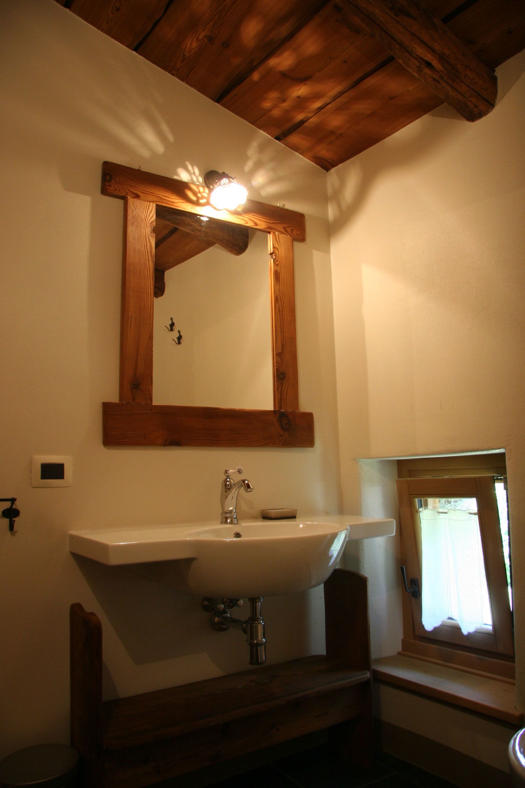 Ein Badezimmer mit Holzboden, einem weißen Waschbecken und einem Spiegel mit Holzrahmen.