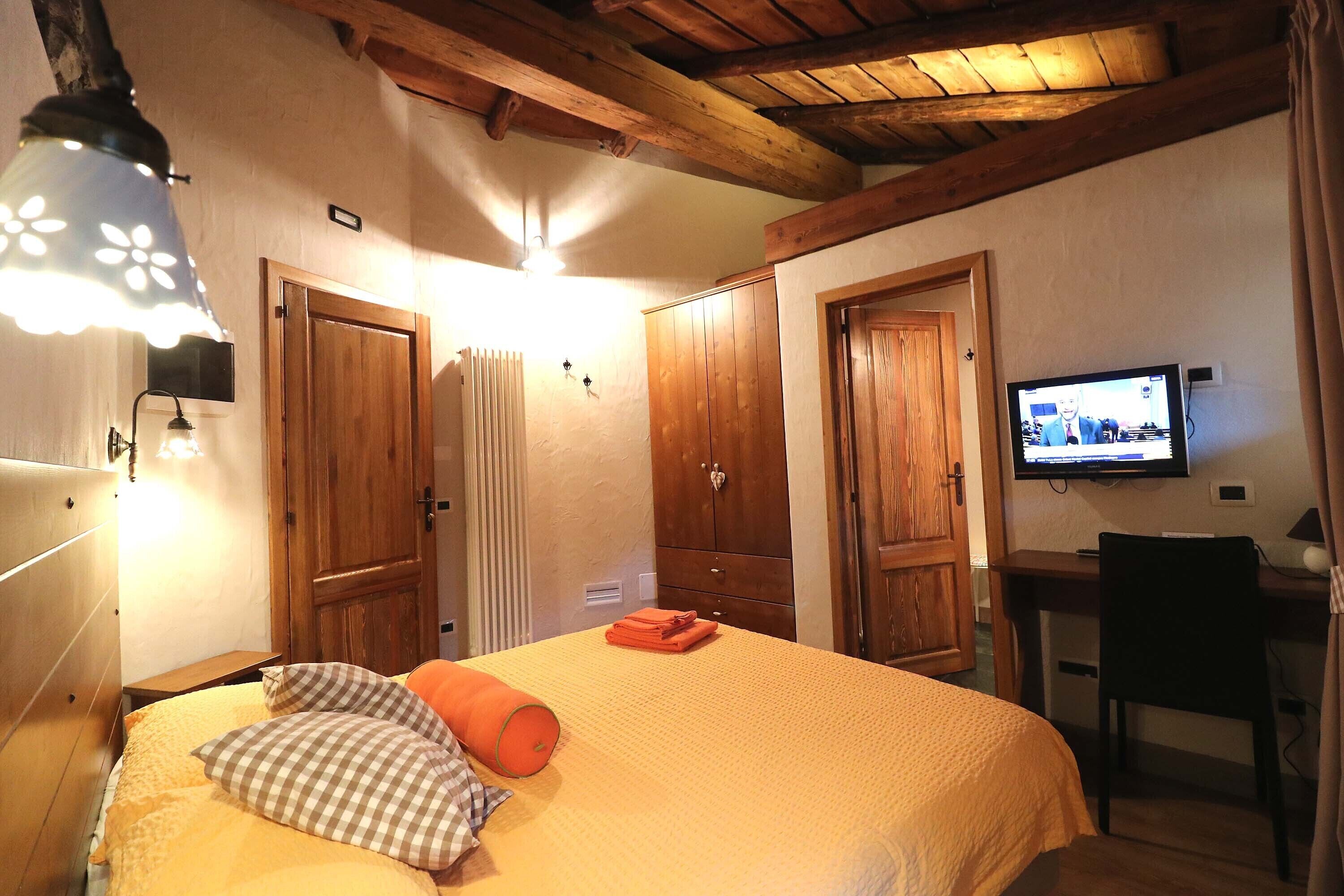 A bedroom with a bed, a desk, a television, and wooden doors.