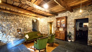 Una habitación rústica con paredes de piedra, un sofá verde, dos sillones, un aparador de madera y una chimenea de piedra.