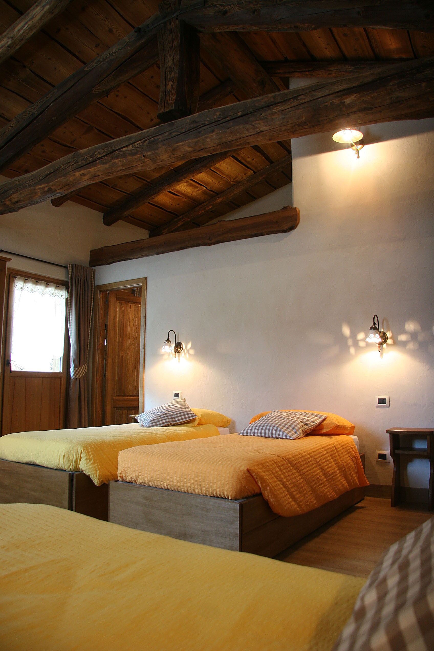 Une chambre avec deux lits, des poutres en bois au plafond et des lampes fixées au mur.