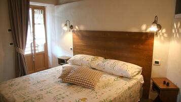 A bedroom with a wooden headboard, floral bedding, two bedside lamps, and a nightstand with a pinecone decoration.