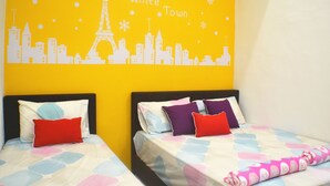 Dos camas con ropa de cama colorida, una pared amarilla con un mural de un paisaje urbano y una almohada roja sobre una de las camas.