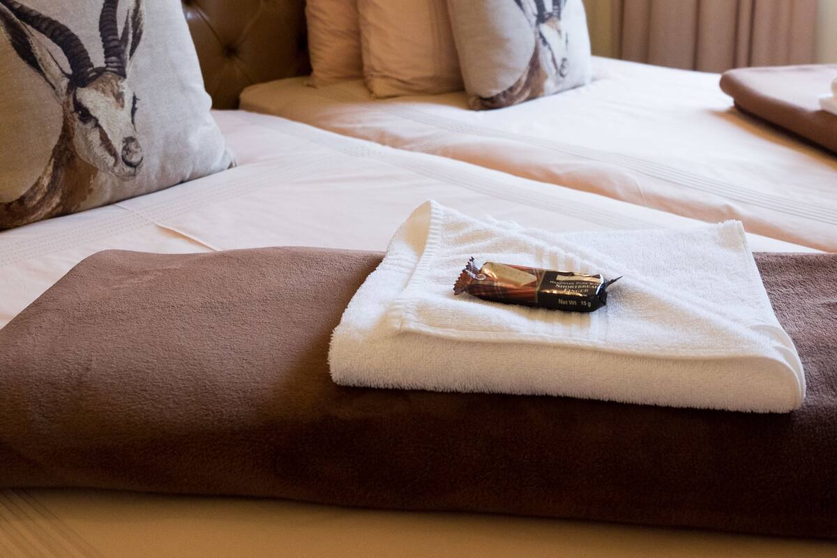 A hotel room with a tufted headboard, a neatly made bed with white linens, and a decorative pillow with an animal design.