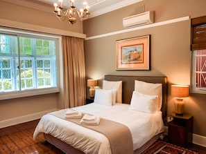 A neatly made bed with white linens and towels, a chandelier, an air conditioning unit, and a framed picture on the wall. - 5 Camp Street Guesthouse & Self-catering (Cape Town)