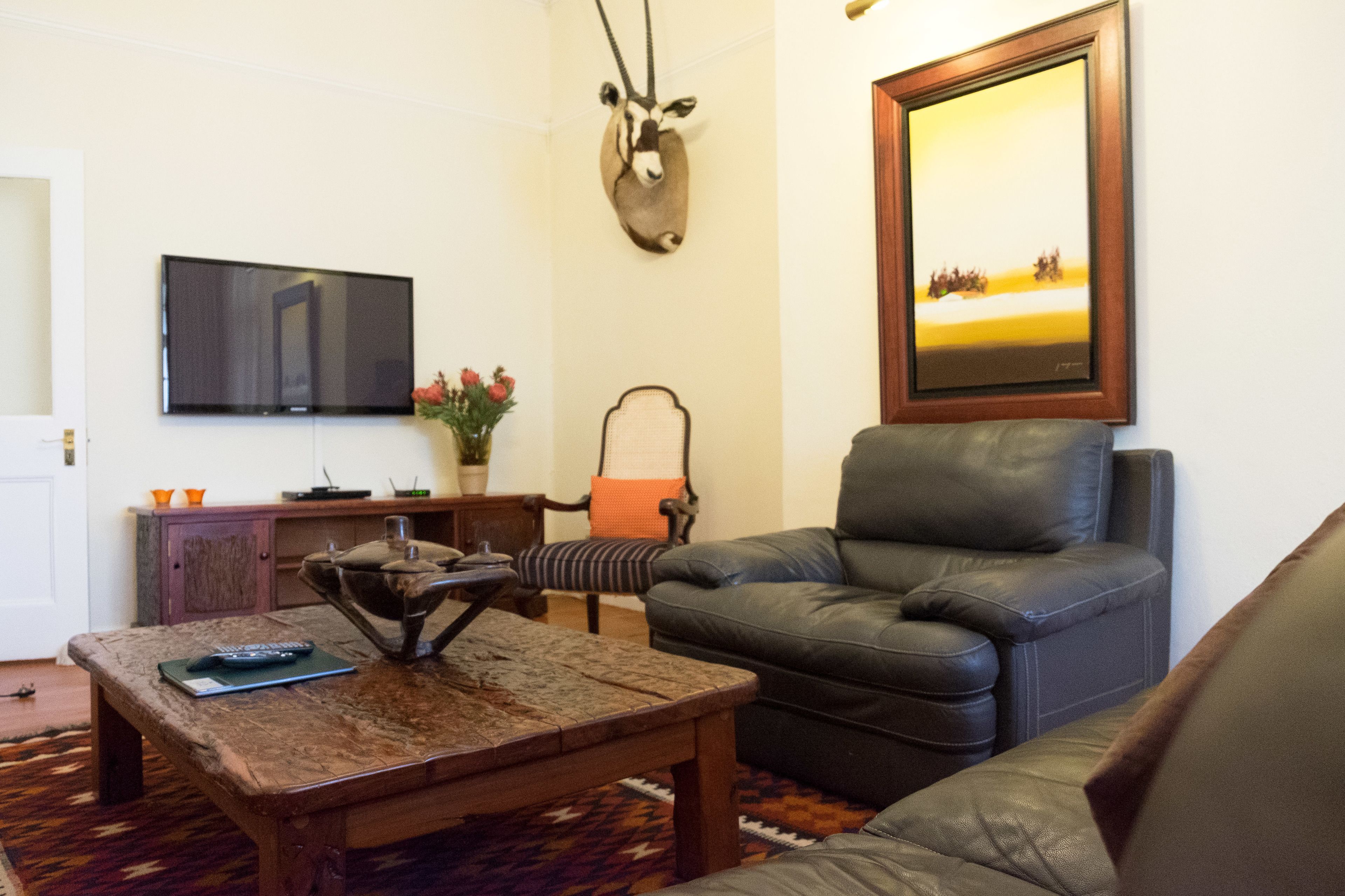 Un salon avec un canapé en cuir, une table basse en bois, un téléviseur fixé au mur et un tableau encadré accroché au mur.