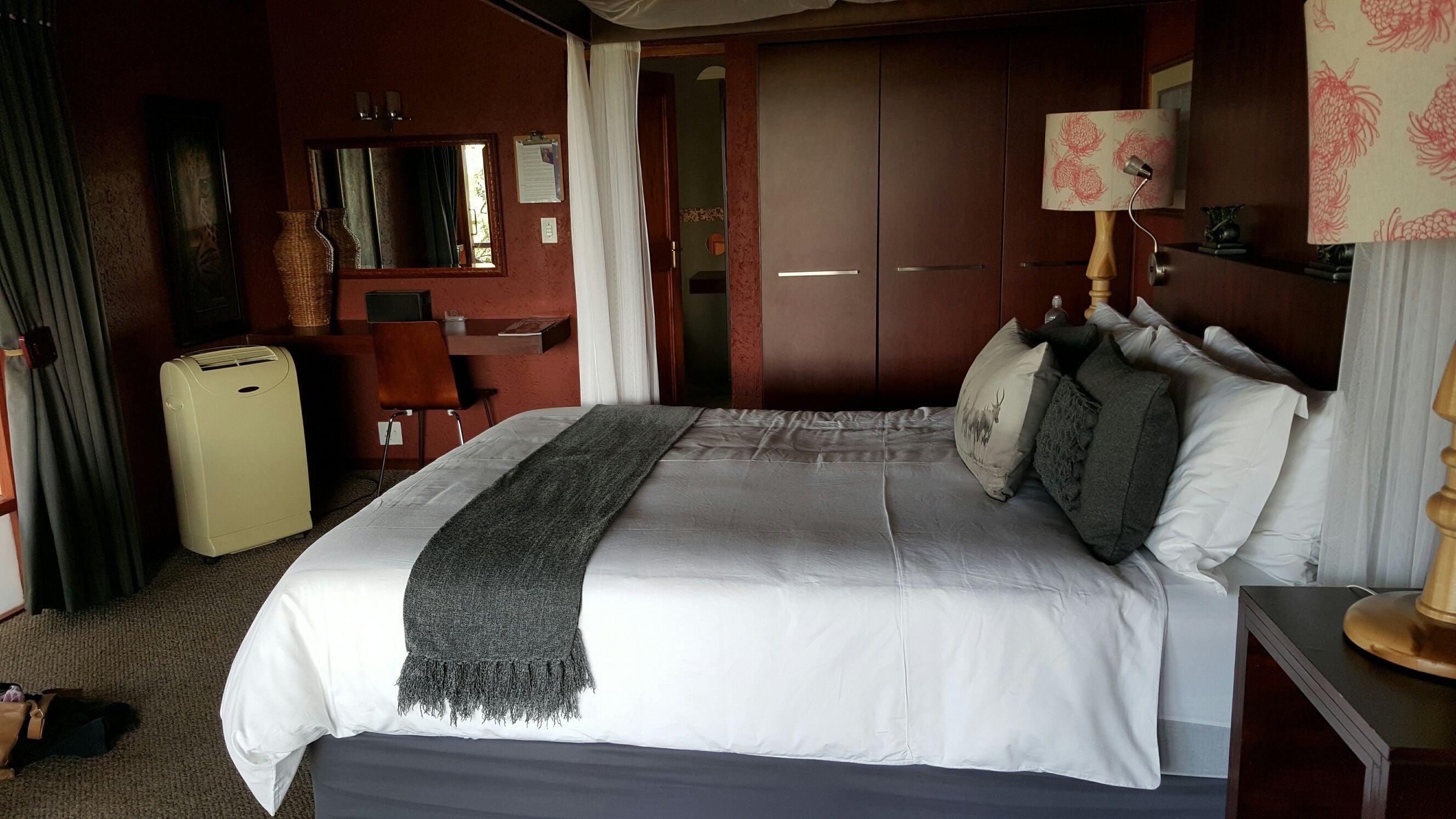Ein Hotelzimmer mit einem großen Bett, einem Schreibtisch, einem Stuhl, einem Kleiderschrank und einer Lampe.
