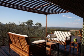 A wooden deck with a wooden bench and a cushioned chair, overlooking a mountainous landscape.