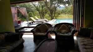 Ein Zimmer mit Korbmöbeln, einem Pool und Blick auf Bäume und Hügel.
